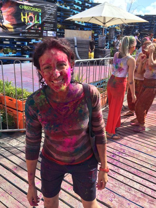 A girl covered head to toe in Holi colours, smiling at the camera