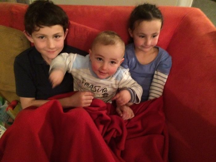Three children sitting together under a red blanket