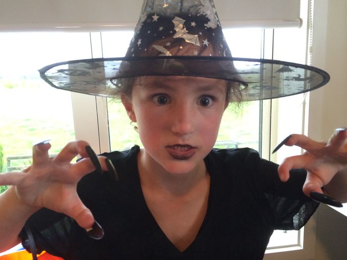 Girl in a black witch hat pulling a spooky face