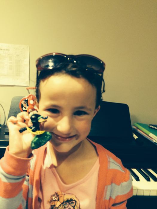Girl at a piano holding a small toy up to the camera